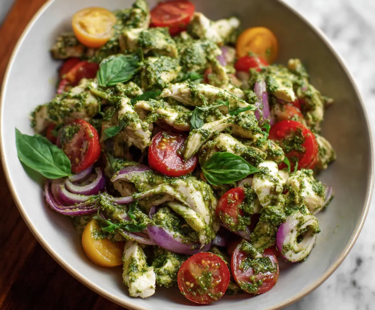 Fresh pesto chicken salad with mixed greens and cherry tomatoes in a glass bowl